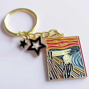 May include: Gold-coloured keyring with a rectangular charm featuring a colourful enamel depiction of Edvard Munch's "The Scream" painting. Includes a black star and a star-shaped charm. A unique accessory.