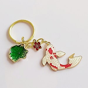 May include: Gold key chain with a red and white koi fish charm, a green lotus leaf charm, and a red flower charm.