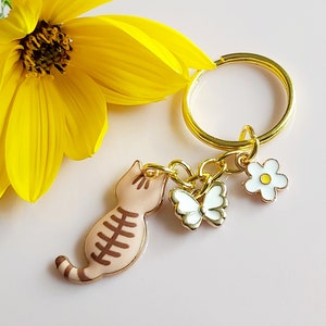 Brown cat keyring. Feline enamel charm keychain with white butterfly and Daisy. Floral cat bag charm. Light brown. Gold tone