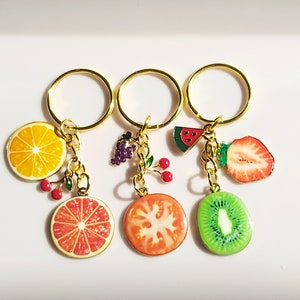 May include: Three gold keychains with fruit charms. The charms are a watermelon, a strawberry, a kiwi, an orange, and a tomato. The keychains are a fun and colorful way to add personality to your keys.