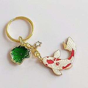 May include: Gold-tone keychain featuring a red and white koi fish charm, a green leaf charm, and a small star charm.