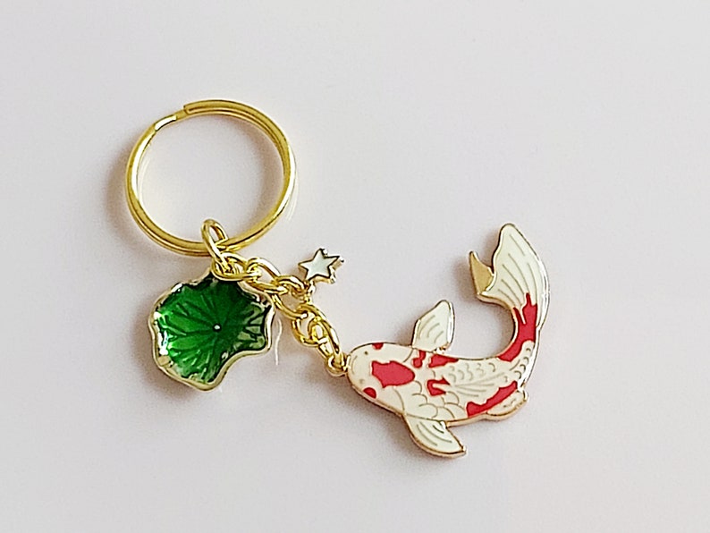 May include: Gold-tone keychain featuring a red and white koi fish charm, a green leaf charm, and a small star charm.