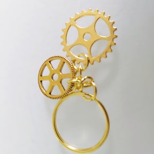 May include: Gold-toned keychain with two gear charms and a circular ring.