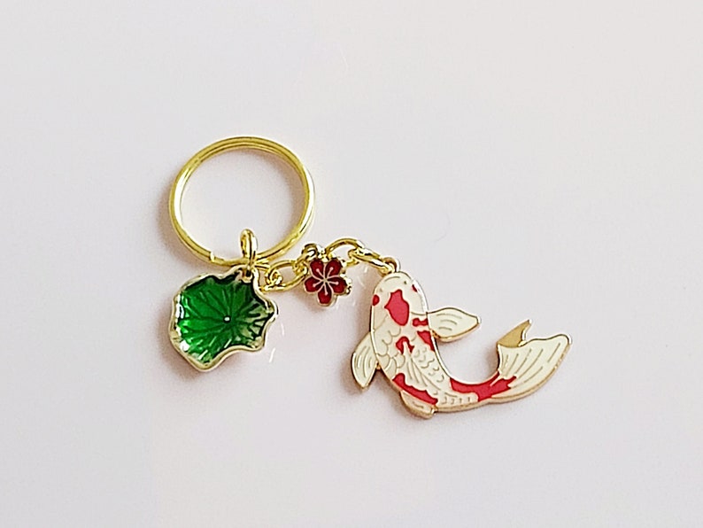 May include: Gold key chain with a red and white koi fish charm, a green lotus leaf charm, and a red flower charm.