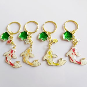 Four gold keychains with a green leaf charm, a small flower charm, and a white and red or yellow koi fish charm.