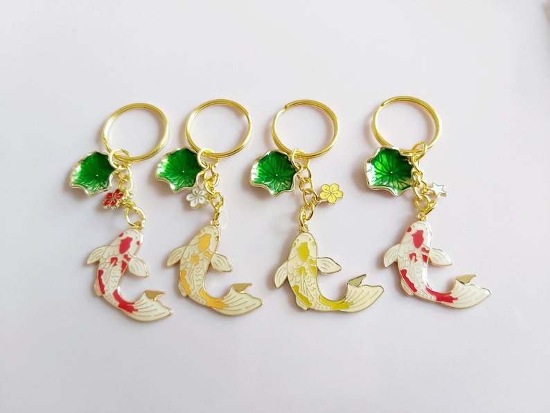 Four gold keychains with a green leaf charm, a small flower charm, and a white and red or yellow koi fish charm.