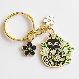 黒猫のキーホルダー。ゴールドトーンのキーホルダーに隠れた花猫と、桜とデイジーのチャーム。かわいい猫好きの方へのプレゼント。