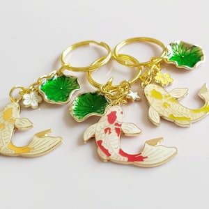 May include: Three gold keychains with charms of koi fish and green lily pads. The koi fish are painted in white, yellow, and red. The lily pads are green with gold accents.