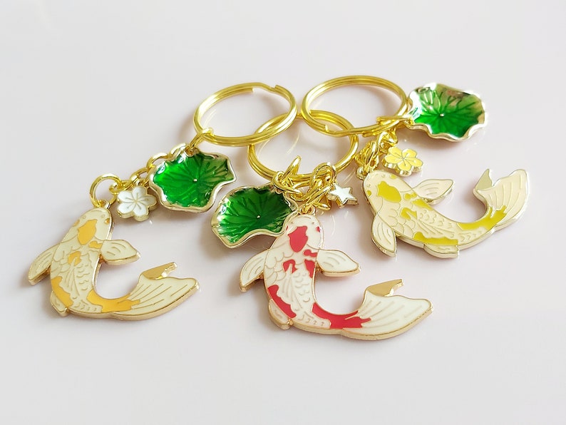 May include: Three gold keychains with charms of koi fish and green lily pads. The koi fish are painted in white, yellow, and red. The lily pads are green with gold accents.