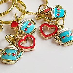 Pode incluir: Cinco chaveiros de ouro com pingentes. Os pingentes são um coração vermelho, um bule azul, um coração vermelho, um bule azul e uma xícara de chá azul com um cartão de jogo vermelho.