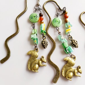 Può includere: Due ciondoli per segnalibri in bronzo con perline a spirale verde e bianco, perline di vetro verde, ciondoli a forma di pigna e ciondoli a forma di scoiattolo.