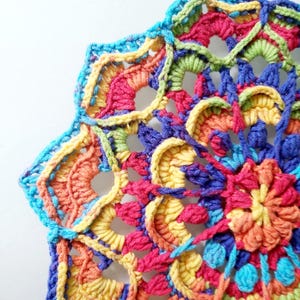 May include: A colourful crocheted mandala with a rainbow pattern. The mandala is made with different shades of blue, green, yellow, orange, and red yarn.