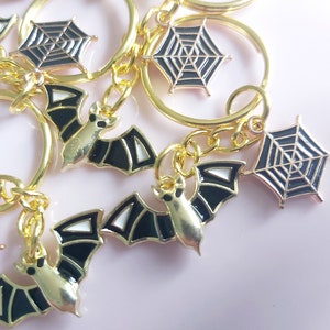 Black bat and spiderweb keyring. Gold tone black enamel bat and cobweb charms on silvertone keychain. Novelty Halloween keychain. Small gift