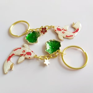 May include: Gold-tone keychain with two white and red koi fish charms, two green lotus leaf charms, and a gold star charm. The keychain also has two gold key rings.