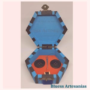 Peut inclure: Bo&icirc;te &agrave; couture hexagonale en bois peinte en bleu avec des rayures noires. &Agrave; l'int&eacute;rieur, deux boutons noirs, une aiguille et du fil reposent sur une base orange. La bo&icirc;te est ouverte, r&eacute;v&eacute;lant son contenu. Le texte "Bluess Artesan&iacute;as" est visible.