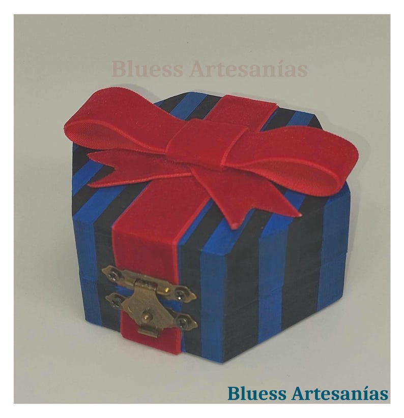 Op de afbeelding: Een kleine, blauw en zwart gestreepte doos met een rode fluwelen strik erop. De doos heeft een messing sluiting en de tekst "Bluess Artesan&iacute;as".