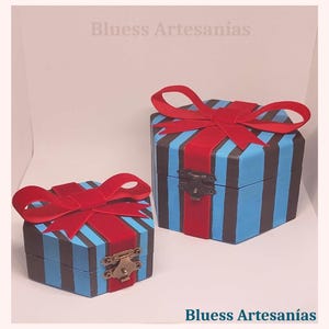May include: Two hexagonal wooden boxes, painted with blue and black stripes, and adorned with red velvet bows. The boxes are secured with metal clasps. The text "Bluess Artesan&iacute;as" is visible.