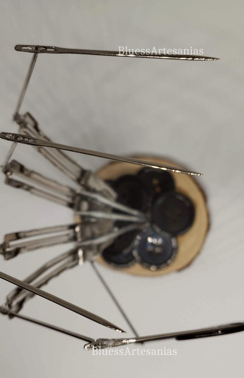 Pu&ograve; includere: Un set di aghi da cucito argentati disposti in un motivo circolare su una base di legno. Gli aghi sono tutti puntati verso l'alto e sono tenuti in posizione da un anello di metallo. La base &egrave; in legno marrone chiaro e ha una finitura naturale.
