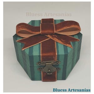 May include: A teal and green striped wooden box with a brown velvet ribbon and bow. The box has a metal clasp and the text "Bluess Artesan&iacute;as". This decorative box is suitable for small gifts or keepsakes.