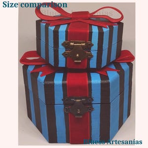 May include: Two hexagonal wooden boxes, one on top of the other, painted with blue and black vertical stripes. Each box has a red ribbon and bow, with a brass clasp closure. The text "Size comparison" is visible.