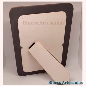 May include: A wooden picture frame with a dark brown border and a light-colored interior. The frame has a built-in stand for display. The text "Bluess Artesan&iacute;as" is visible on the frame.