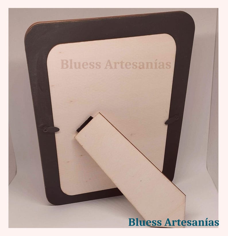 May include: A wooden picture frame with a dark brown border and a light-colored interior. The frame has a built-in stand for display. The text "Bluess Artesan&iacute;as" is visible on the frame.