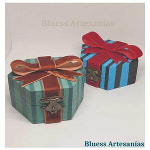 May include: Two decorative wooden boxes with lids. One is teal with brown stripes and a brown velvet bow. The other is blue with red stripes and a red velvet bow. Both have metal clasps. The text "Bluess Artesan&iacute;as" is visible.