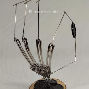 Pu&ograve; includere: Una scultura in metallo argentato di una mano che tiene un mucchio di bottoni neri. La scultura &egrave; su una base di legno. La scultura &egrave; intitolata "BluessArtesanias".