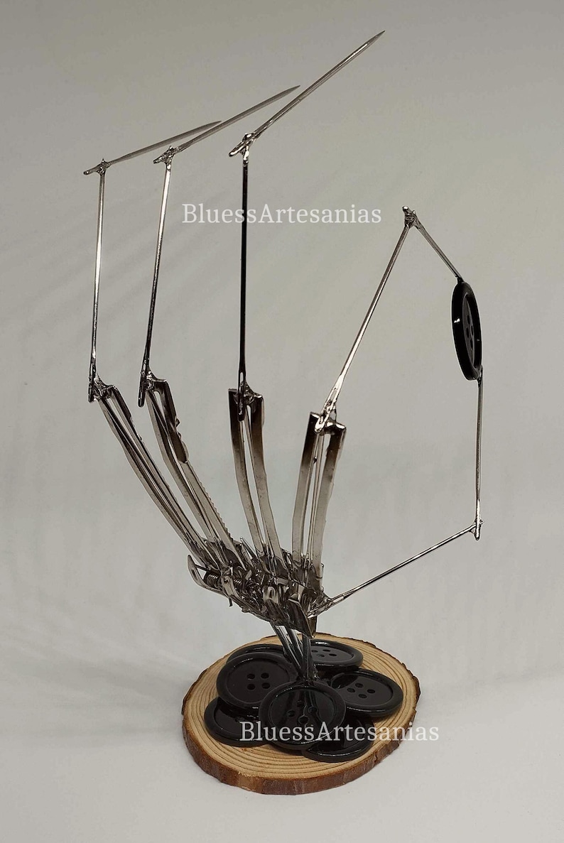 Pu&ograve; includere: Una scultura in metallo argentato di una mano che tiene un mucchio di bottoni neri. La scultura &egrave; su una base di legno. La scultura &egrave; intitolata "BluessArtesanias".