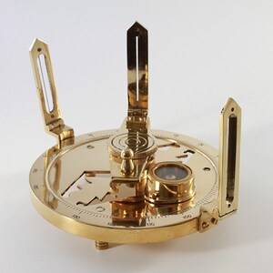 May include: A brass compass with a compass needle, a protractor, and a sighting device. The compass is marked with numbers from 0 to 180 degrees.