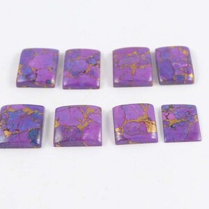 May include: Eight square-shaped gemstones with rounded corners. The stones feature a vibrant purple hue with intricate gold and blue veining patterns. The gemstones are arranged on a white surface, showcasing their unique color and texture.