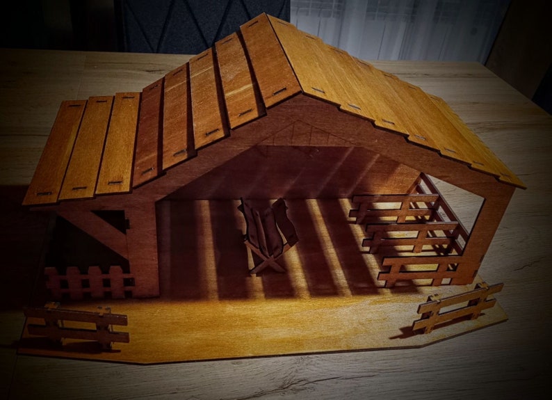 May include: A wooden nativity scene with a brown roof and a manger inside. The scene is made of wood and has a rustic look.