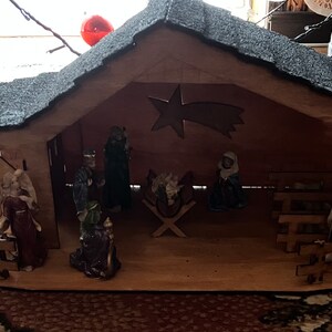 May include: A wooden nativity scene with figurines of Mary, Joseph, and the baby Jesus. The scene also includes a star, a manger, and a fence. The figurines are made of ceramic and are painted in realistic colors.