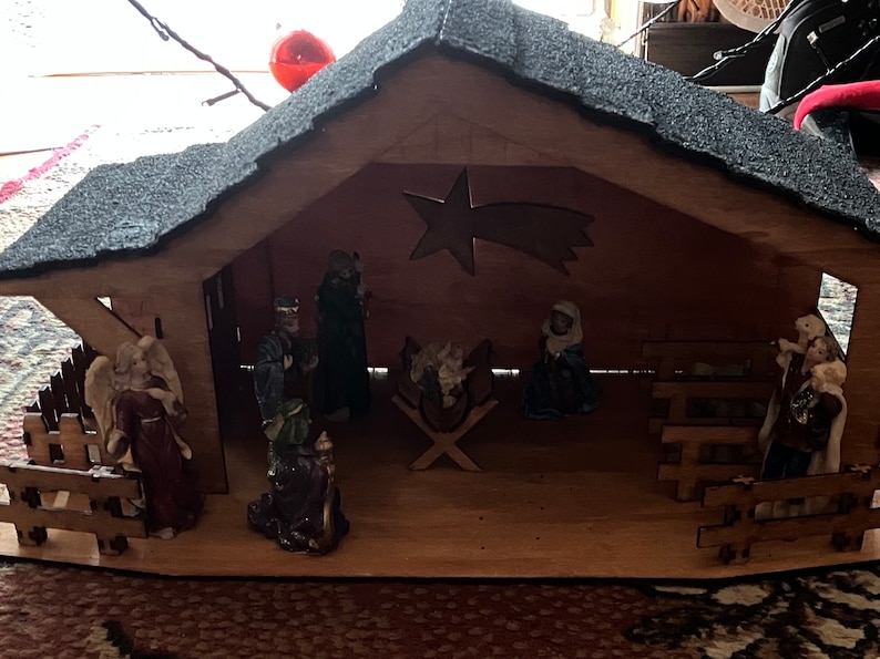 May include: A wooden nativity scene with figurines of Mary, Joseph, and the baby Jesus. The scene also includes a star, a manger, and a fence. The figurines are made of ceramic and are painted in realistic colors.