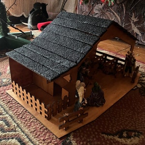 May include: A wooden nativity scene with a black shingled roof, a brown wooden fence, and figurines of Mary, Joseph, and the baby Jesus.