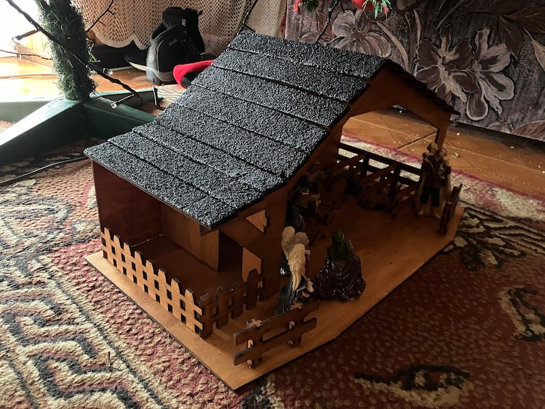 May include: A wooden nativity scene with a black shingled roof, a brown wooden fence, and figurines of Mary, Joseph, and the baby Jesus.
