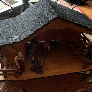May include: A wooden nativity scene with a black felt roof. The scene includes figures of Mary, Joseph, baby Jesus, and the three wise men. The figures are made of painted wood and have a rustic look.