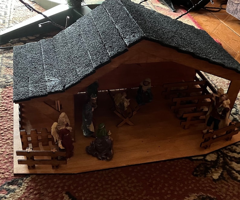 May include: A wooden nativity scene with a black felt roof. The scene includes figures of Mary, Joseph, baby Jesus, and the three wise men. The figures are made of painted wood and have a rustic look.
