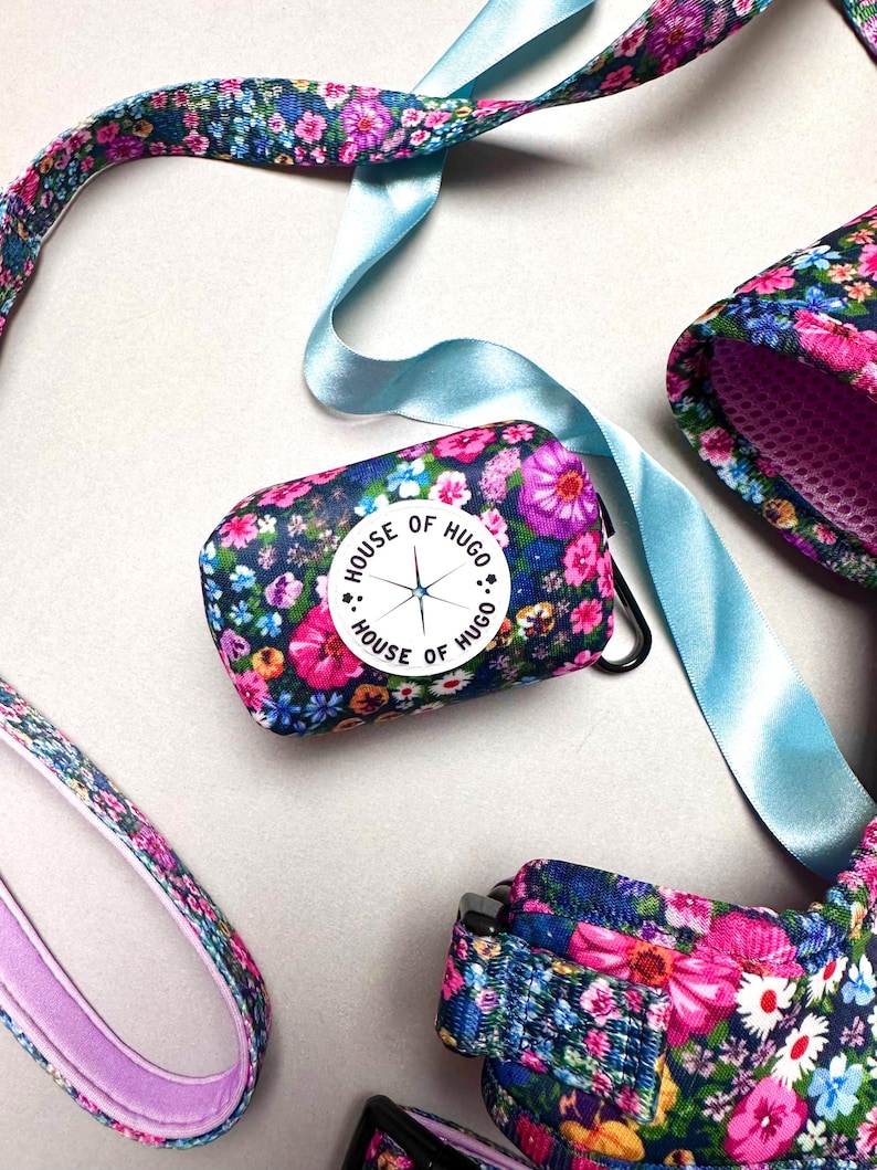 Puede incluir: Un juego de correa y collar para perro con estampado floral y un porta bolsas para excrementos a juego. El porta bolsas para excrementos tiene un c&iacute;rculo blanco con el texto "House of Hugo" y un dise&ntilde;o de br&uacute;jula.