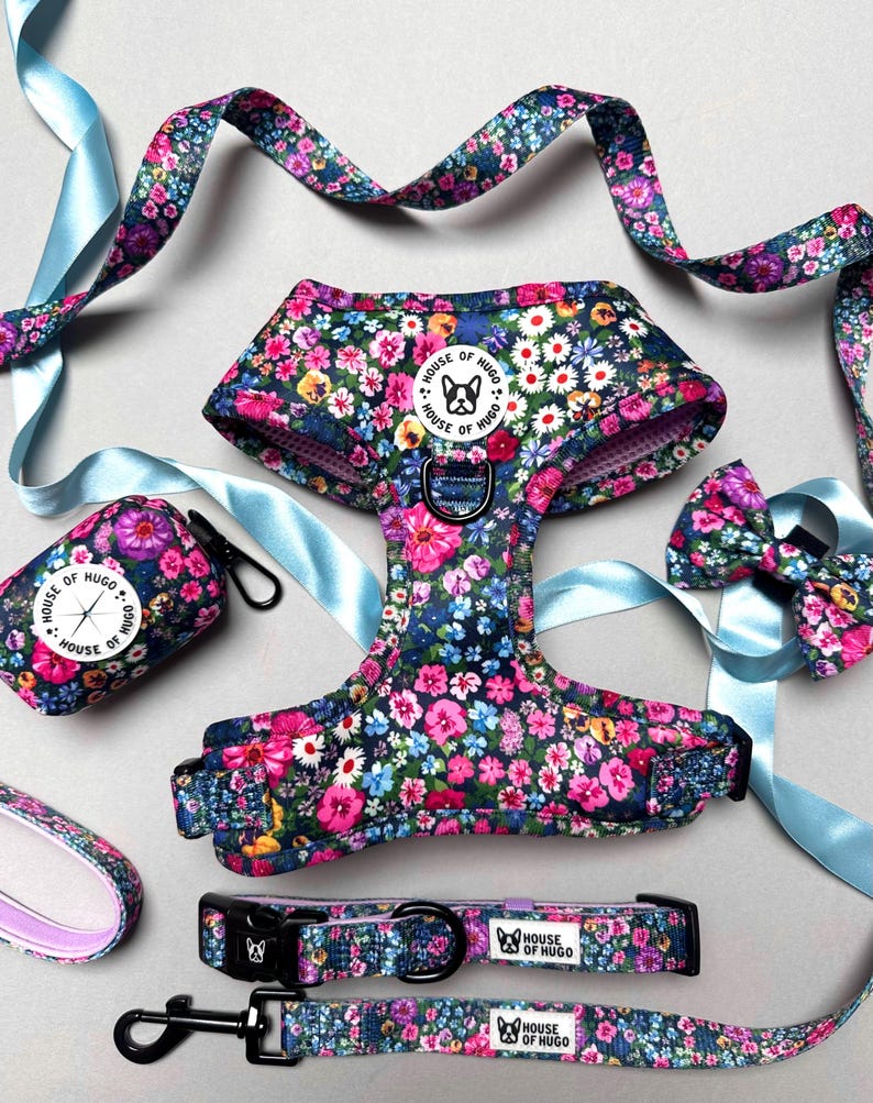 Puede incluir: Un conjunto de arn&eacute;s, correa y porta bolsas para perros con estampado floral. El arn&eacute;s y la correa son de color azul marino con un estampado floral rosa y blanco. El porta bolsas es de color azul marino con un estampado floral blanco y el texto "House of Hugo".