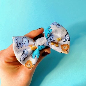 Könnte beinhalten: Eine weiße Schleife mit einem blauen und gelben Tierdruck. Die Schleife zeigt verschiedene Tiere, darunter Elefanten, Zebras, Löwen und Nashörner.