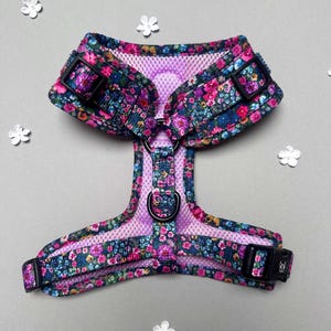Puede incluir: Un arn&eacute;s para perro floral con forro de malla rosa y hebillas negras. El arn&eacute;s tiene un patr&oacute;n floral con flores rosas, azules y amarillas.