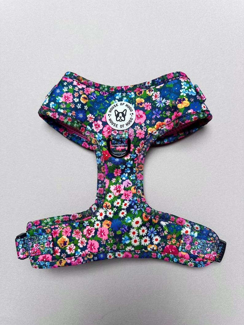 Puede incluir: Un arn&eacute;s para perro azul y rosa con estampado floral, con una hebilla negra ajustable y un logotipo circular blanco que dice "House of Hugo".