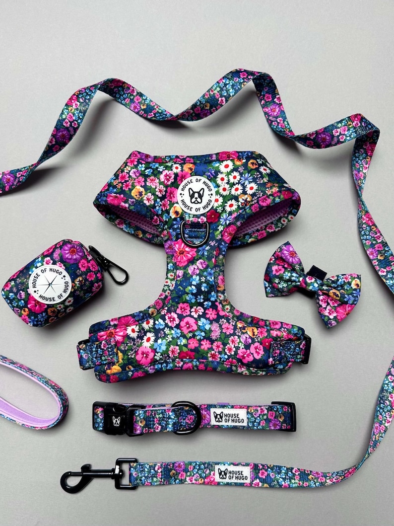 Puede incluir: Un conjunto de arn&eacute;s, correa, collar y portador de bolsas para perros con estampado floral. El conjunto es de color azul y rosa floral con un logotipo en blanco y negro que dice "House of Hugo".