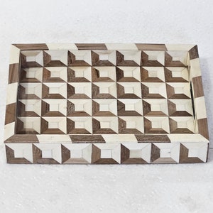 May include: A rectangular tray with a geometric pattern made of bone and wood. The tray has a light brown wood frame and a white and brown geometric pattern inside.