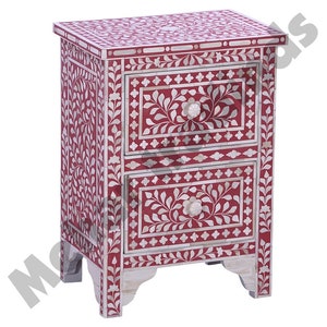 May include: A red wooden nightstand with two drawers, both decorated with white floral patterns and bone inlay. The nightstand has a floral design on the front and sides.