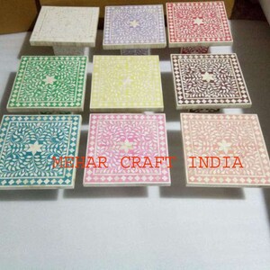 May include: A set of nine square bone inlay tables with intricate floral designs in various colors, including green, yellow, pink, purple, and red. The tables are made of white marble and have a polished finish.