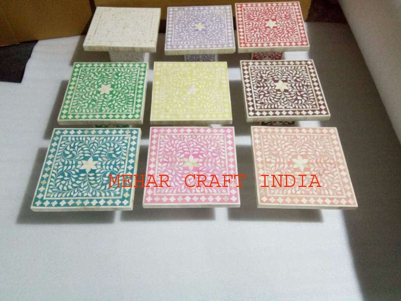 May include: A set of nine square bone inlay tables with intricate floral designs in various colors, including green, yellow, pink, purple, and red. The tables are made of white marble and have a polished finish.
