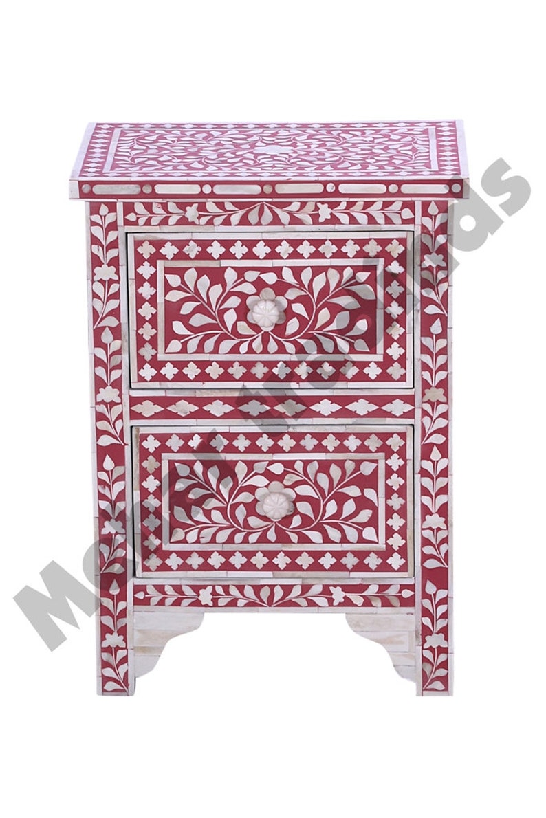 May include: A red wooden nightstand with two drawers. The drawers are decorated with white floral patterns and intricate bone inlay. The nightstand has a traditional design and is perfect for adding a touch of elegance to any bedroom.