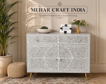 May include: A rectangular gray cabinet featuring intricate white floral inlay patterns, one top drawer, and two lower doors with small round knobs. The piece is supported by four slender gold-toned metal legs and displays the text MEHAR CRAFT INDIA.